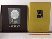 Two books side by side: one dark brown 'Paramyths: Sculpture' with a white stylized sculpture on cover, and one yellow hardcover 'Max Ernst' with black illustration and text