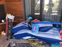 Photo showing pool toys and accessories including inflatable mattress, pool noodles, inflatable ball, boogie board, and pumps piled together.