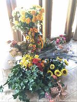 Multiple assorted faux flower arrangements, including sunflowers, yellow, orange, and purple flowers, and faux ivy laid on floor.