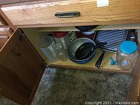 Bottom cabinet with pitchers, frying pan, colander, glass jar with lid, and various pots.