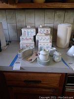 Four southwest-style ceramic canisters with lids, cream and sugar set, demitasse cups and saucers and small ceramic spoon rest arranged on countertop.