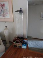 Tall hexagonal glass aquarium with black base, aquarium supplies on top and nearby box with tubing.