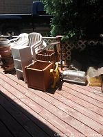 Photo of five wooden plant stands and various garden supplies on a deck, showing plastic plant starters, a yellow plant roller, and metal/clear plastic containers.