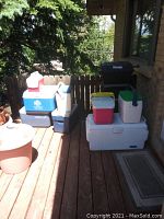 Photo showing all coolers stacked and arranged outdoors on a wooden deck, including a round beige cooler on the left and taller white/green cooler on the right.