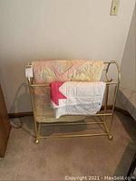 Front view of brass-colored quilt rack with two quilts draped over it, showing size and color details.