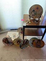 Seven collector plates and vintage wood table showing overall lot