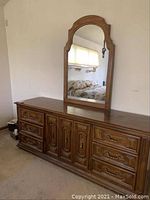 Full view of wooden dresser with mirror showing nine drawers and arched mirror.