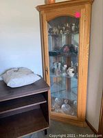 Full view of oak corner cabinet with glass door and contents next to dark wood bookcase with open shelf.