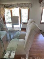 Photo of multiple ivory-colored upholstered dining chairs placed near a glass table and window showing the fabric and chair style.