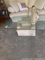 Photo of the glass coffee table showing the glass top and stone base from a side angle in a living room setting.