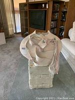 Front view of white ceramic Native American style sculpture with yarn and beads on a stone pedestal.