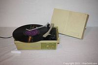 Overall side view of mid-century modern portable record player with spun vinyl record on the turntable and open hinged cover.