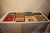 Top view of 12 vinyl LP albums displaying a range of classic rock and folk artists on their covers, laid out on a white table cloth.