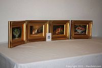 Four framed oil paintings positioned standing on a table showing overall view with visible frames and painting details.