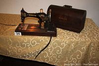 Full view of the Singer sewing machine on wooden base next to its bentwood wooden case with handle.