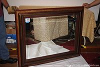 Large beveled rectangular mirror with dark wood frame being held upright by two people, showing overall size and style.