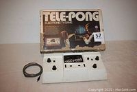 Photo of the Tele-Pong electronic TV game console in white plastic housing with black knobs. Box is behind the console showing a family setup playing the game. RCA cable beside the console.