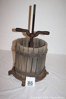 Full view of the vintage apple press showing wooden slats with iron bands, cast iron base, and screw handle on top