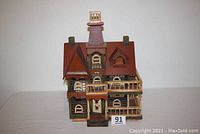 Front view of the colorful Victorian style vintage bird house showing the roof, chimney, windows, and front porch