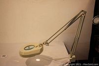 Lighted magnifier mounted on articulated arm showing side profile and illuminated lens.