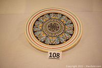 Top view image of ceramic platter showing circular intricate hand painted and decal ornaments in blue, yellow, green, purple colors with a small chip on the edge.