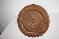 Front view of round wooden plate with intricate carved designs and small colored inlays.