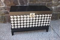 Front view of rectangular wooden blanket chest showing black and white houndstooth geometric pattern, black top and base, and metallic lock plate.