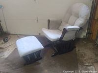 Full view of the gray upholstered Windsor glider rocking chair with matching ottoman on a textured mat in a garage.