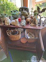Overview of shelf with various animal figurines including frogs, cat, squirrel, bat, turtle; baskets with plate inside, scissors visible.