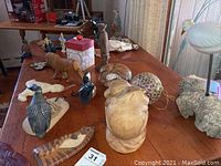 Table with animal figurines including wooden carved monkey, bird figurines, and other animal shapes
