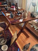 Full view of the wood table, showing the rectangular top and various decorative items placed on it. The table stands on an X-frame base and is placed on a hardwood floor with a rug.