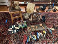 Overview of the lot showing wooden stool, doll bench, lamp with fabric shade, monkey figurine, squirrel sign, wall clock, bowls, and multiple wooden bird decorations arranged on carpet.