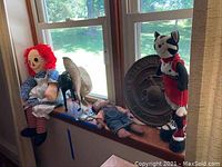 Photo showing Raggedy Ann doll with red yarn hair, plastic horse, cowboy hat, US Marine metal plate, and a cat doll on a window ledge.
