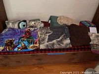 Overview of six assorted blankets and throws with various patterns and colors laid out on a bench or daybed.