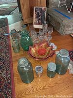 Overview of lot including several blue-green vintage canning jars with metal lids, stemmed glasses, decorative bowls, and the Soda King soda syphon box at the back.
