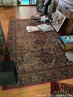 Full view of the wool pile area rug spread on a wood floor, showing the central medallion pattern and overall condition.