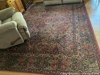 Full view of large oriental-style area rug placed in living room with armchair and couch partly on top of it.