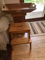 Wooden tray, wooden stepladder, and wooden storage cabinet arranged near a window on a hardwood floor with carpet.