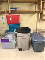 Plastic bins and waste can arranged on floor and shelving, showing various bins stacked and lids stored separately.