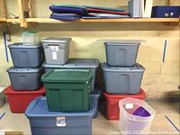 Stack of assorted plastic storage bins in multiple colors including gray, red, green, and clear with lids and labels visible