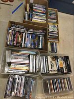 Boxes and bins filled with numerous DVDs and CDs showing wide variety of titles and music genres.