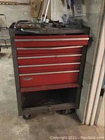 Full view of red Craftsman tool chest showing bent drawers and open bottom shelf, on wheels