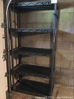 Dark gray plastic shelving unit with five slatted shelves against cinder block wall in garage.