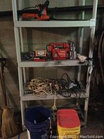 Image showing plastic shelving with red Husky battery charger, sprayer, coiled rope, hardware items, insulation, and buckets below
