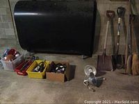 Wide shot showing black tank, plastic bins with clamps and work lights, metal fixture, shovels, brooms, and other hand tools.