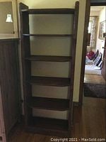 Full view of tall dark wood bookshelf with five shelves and metal hooks on side.