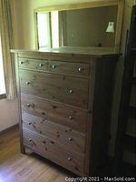 Full view of wooden dresser with five drawers topped by a framed wall mirror.
