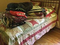 Bed with patchwork star pattern quilt laid out, topped with several folded blankets of various designs including red fleece and animal print.