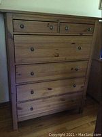 Front view of a tall wooden dresser with multiple drawers and metal knobs.