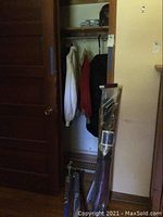 Photo of golf clubs and umbrella in plastic bag inside closet with garment bag and hanging jackets
